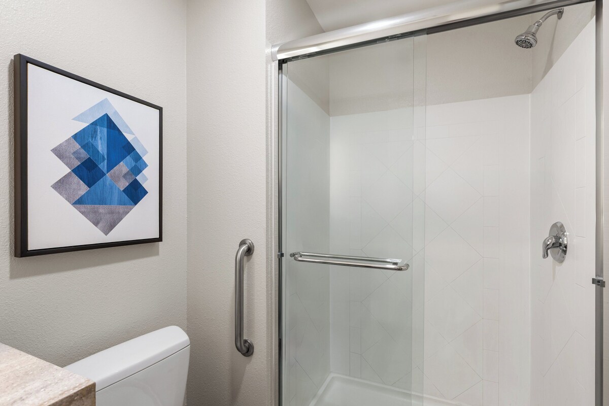 A glass-enclosed shower with a handheld showerhead, a glass door, and a framed abstract painting on the wall.