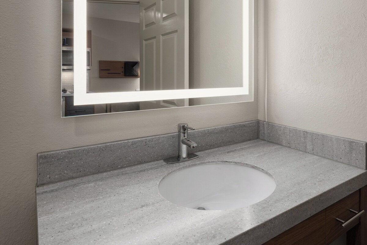 A bathroom with a granite countertop, a white sink, a modern faucet, and a mirror with a light.