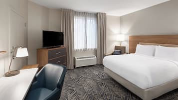 A hotel room with a bed, a desk with a chair, a television, a lamp, and a window with curtains.