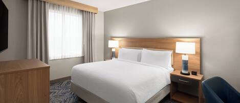 Habitación de hotel con una cama grande, dos mesitas de noche con lámparas, un cabecero de madera, un escritorio y una silla.