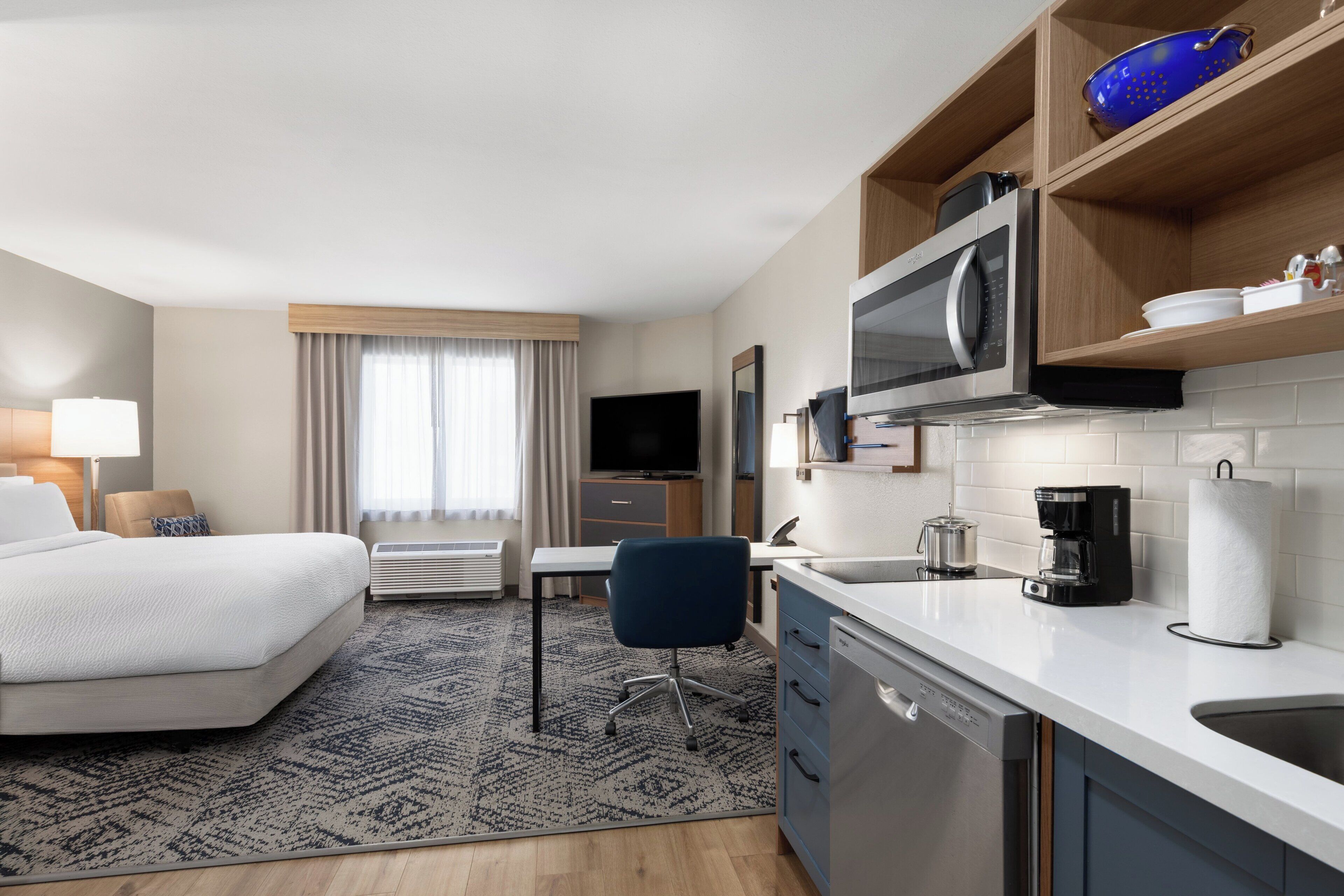 A hotel room with a bed, desk, kitchenette, and a TV.