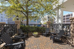 Un patio exterior con cuatro sillas Adirondack, una jardinera grande con follaje y una valla de hierro forjado.