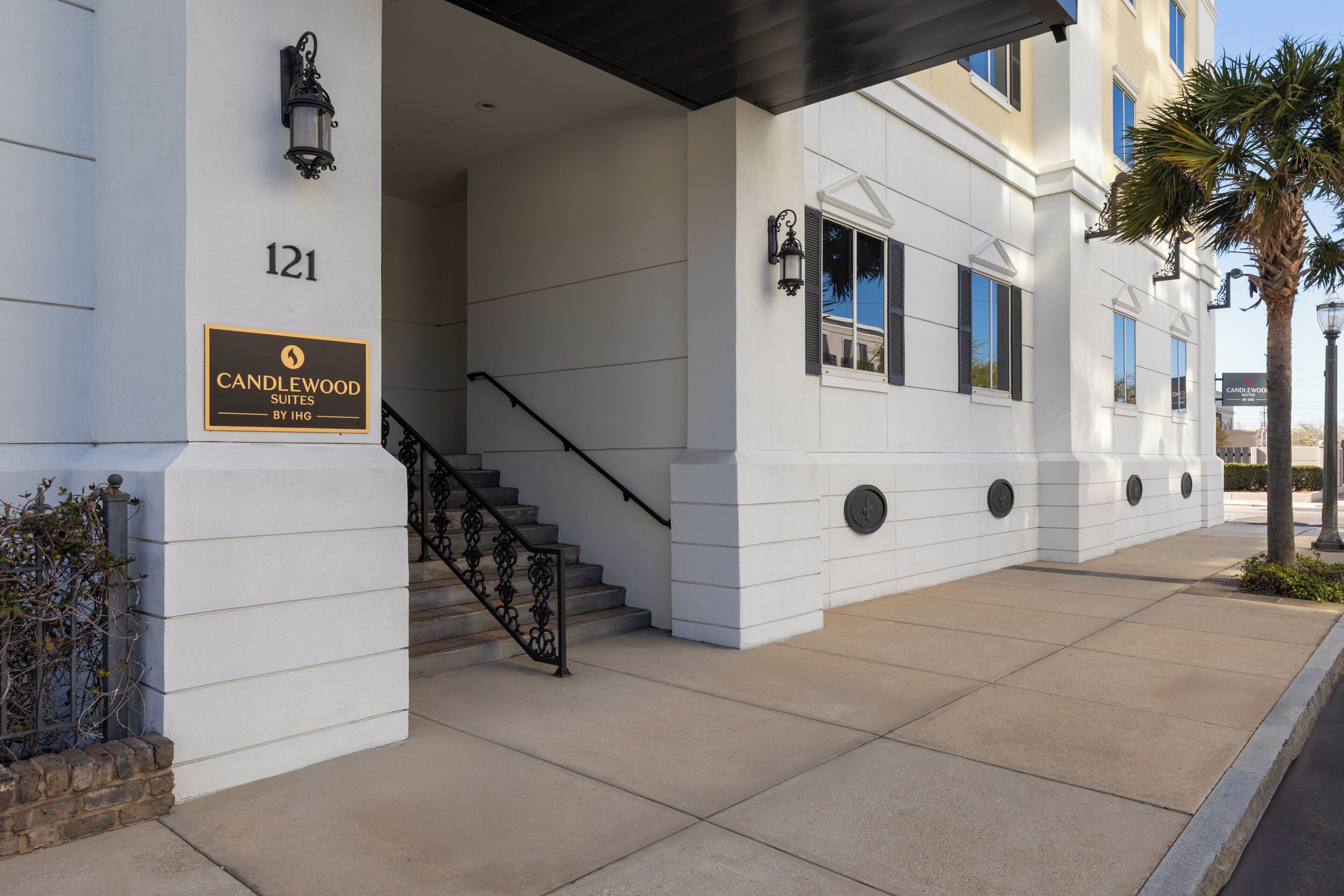 A building entrance with a sign for Candlewood Suites by IHG, a staircase, and a palm tree.