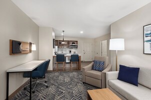 Una habitación de hotel moderna con zona de comedor, kitchenette y un sofá sobre un tapete estampado.