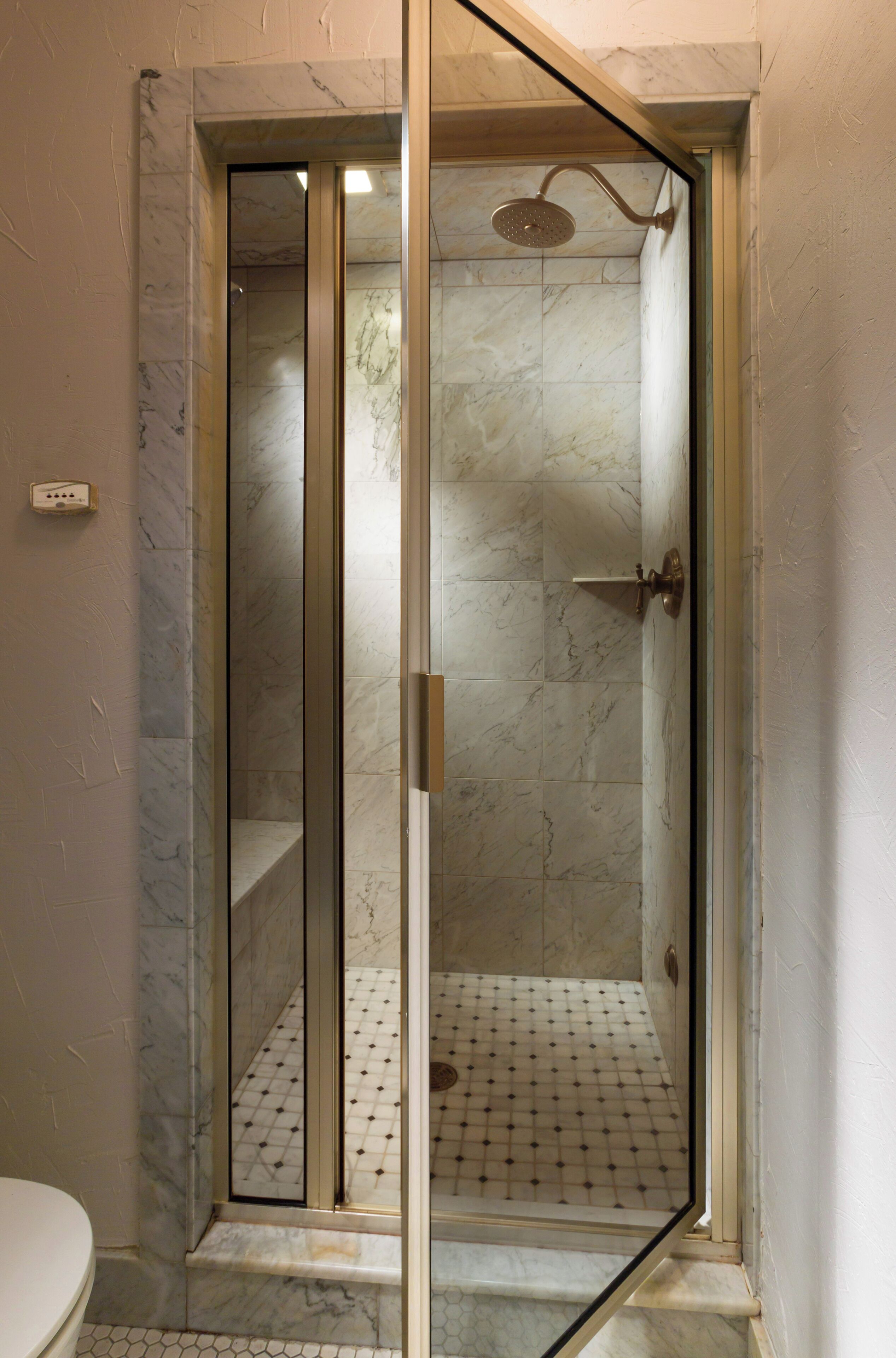 A glass-enclosed shower with a marble floor and a door with a handle.