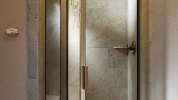 A glass-enclosed shower with a marble floor and a door with a handle.