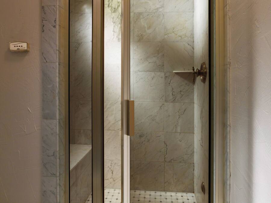A glass-enclosed shower with a marble floor and a door with a handle.