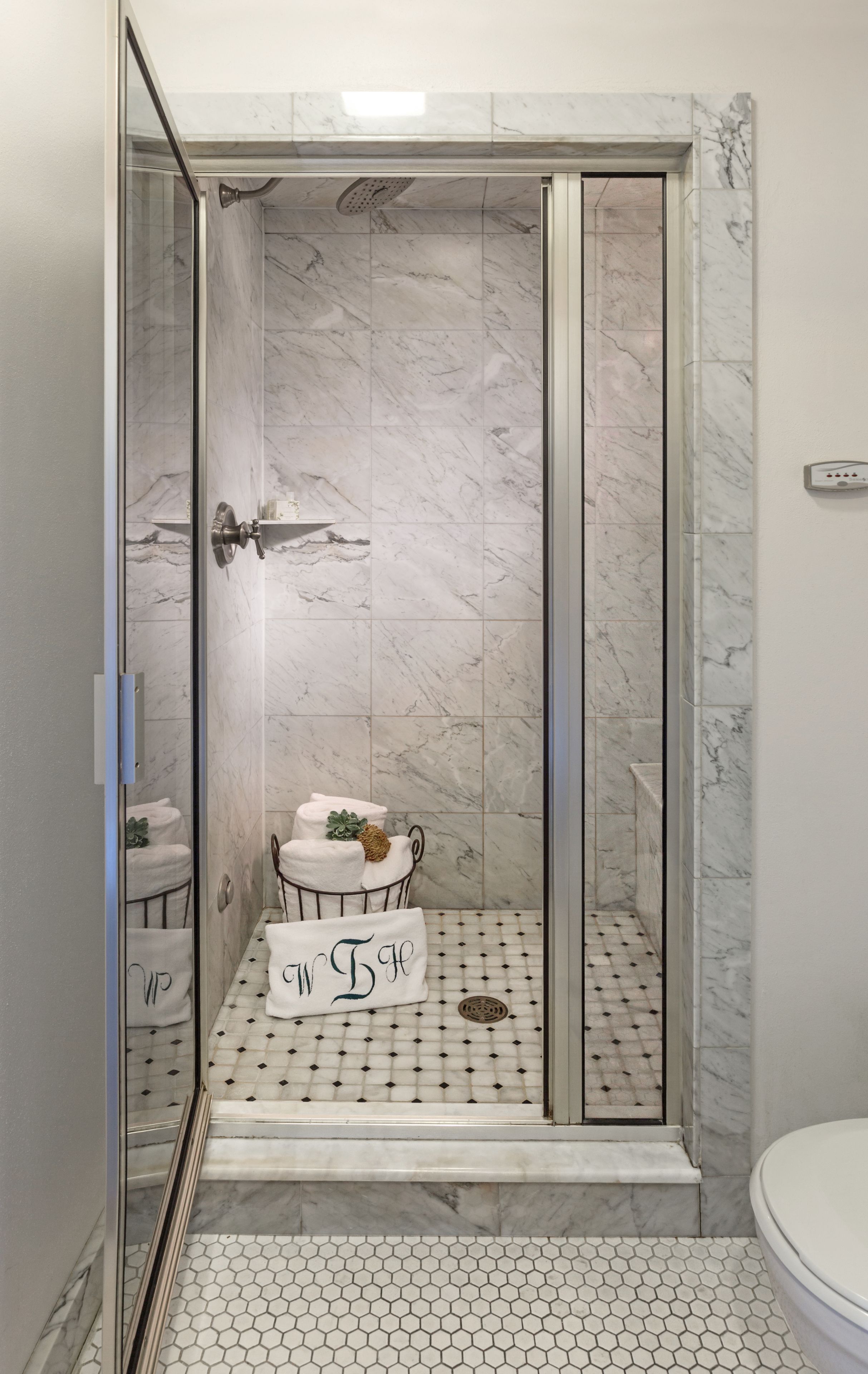 A shower with a glass door, marble walls, and a tiled floor.