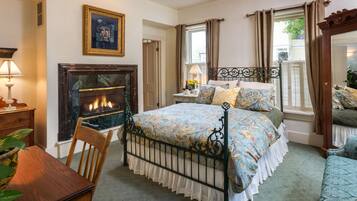 A bedroom with a bed, a fireplace, a nightstand, a chair, and a window with curtains.