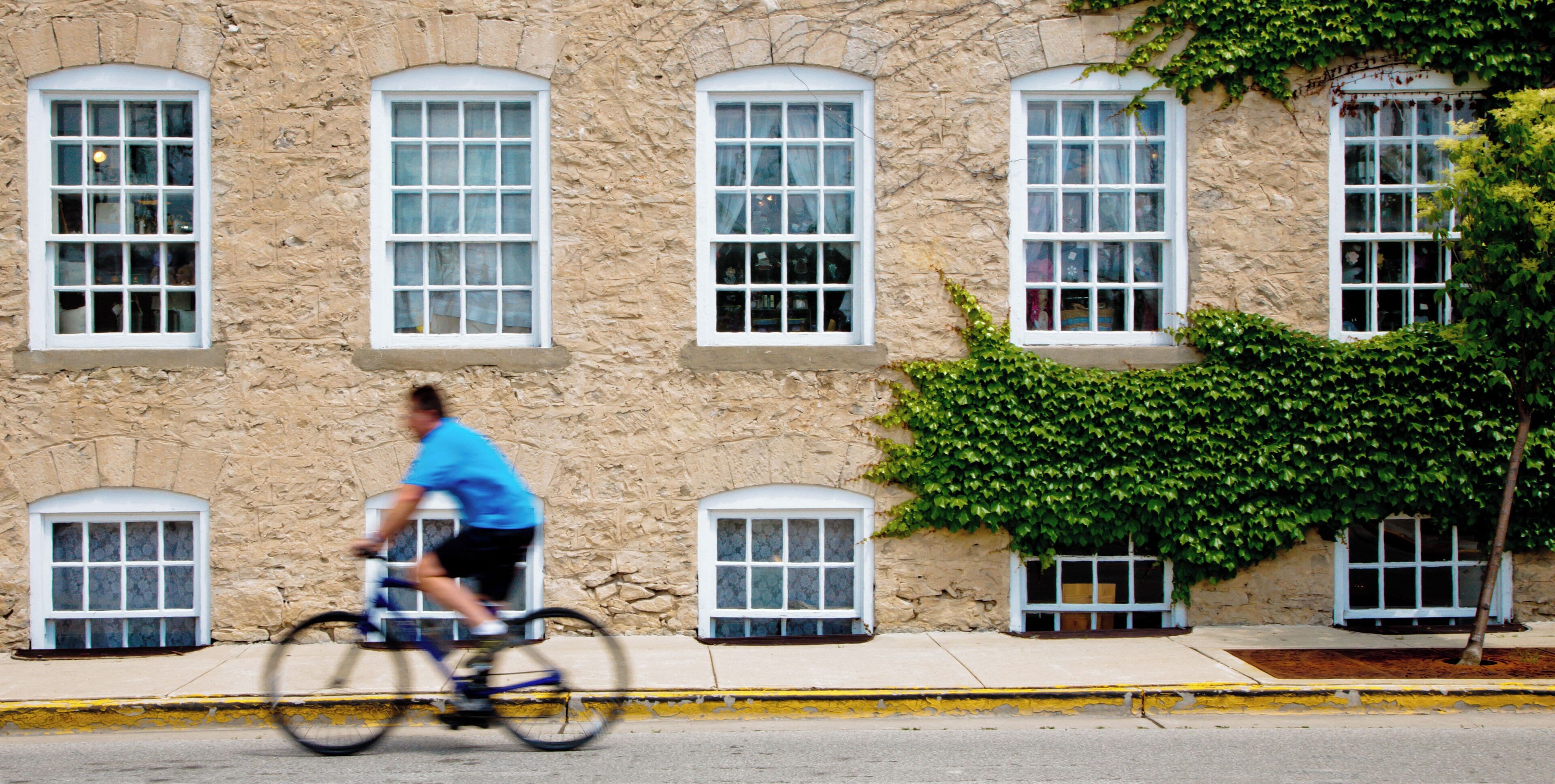 A stone building with multiple windows and a cyclist riding past.