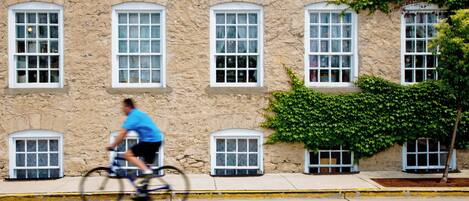 A stone building with multiple windows and a cyclist riding past.