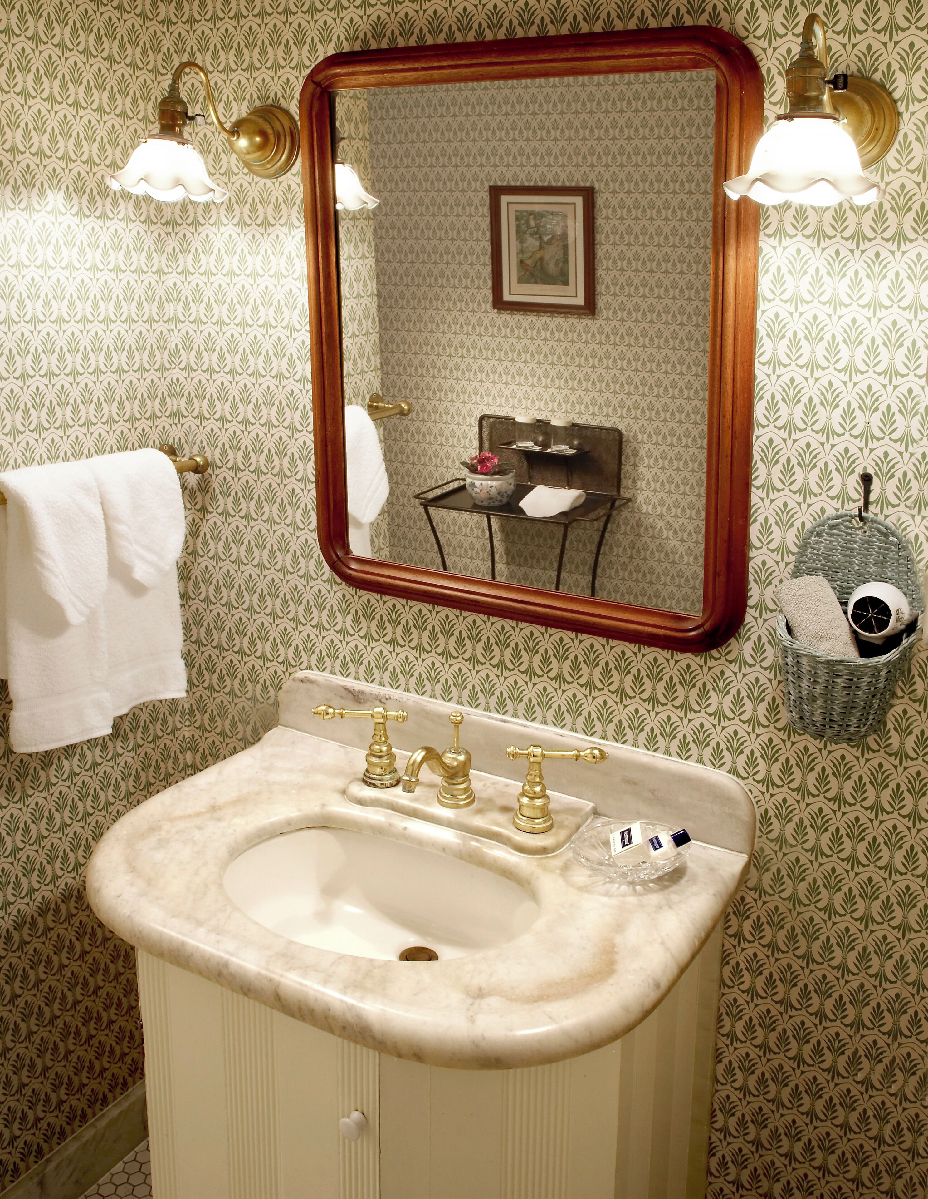 A bathroom with a marble sink, gold faucets, and a mirror with a wooden frame.