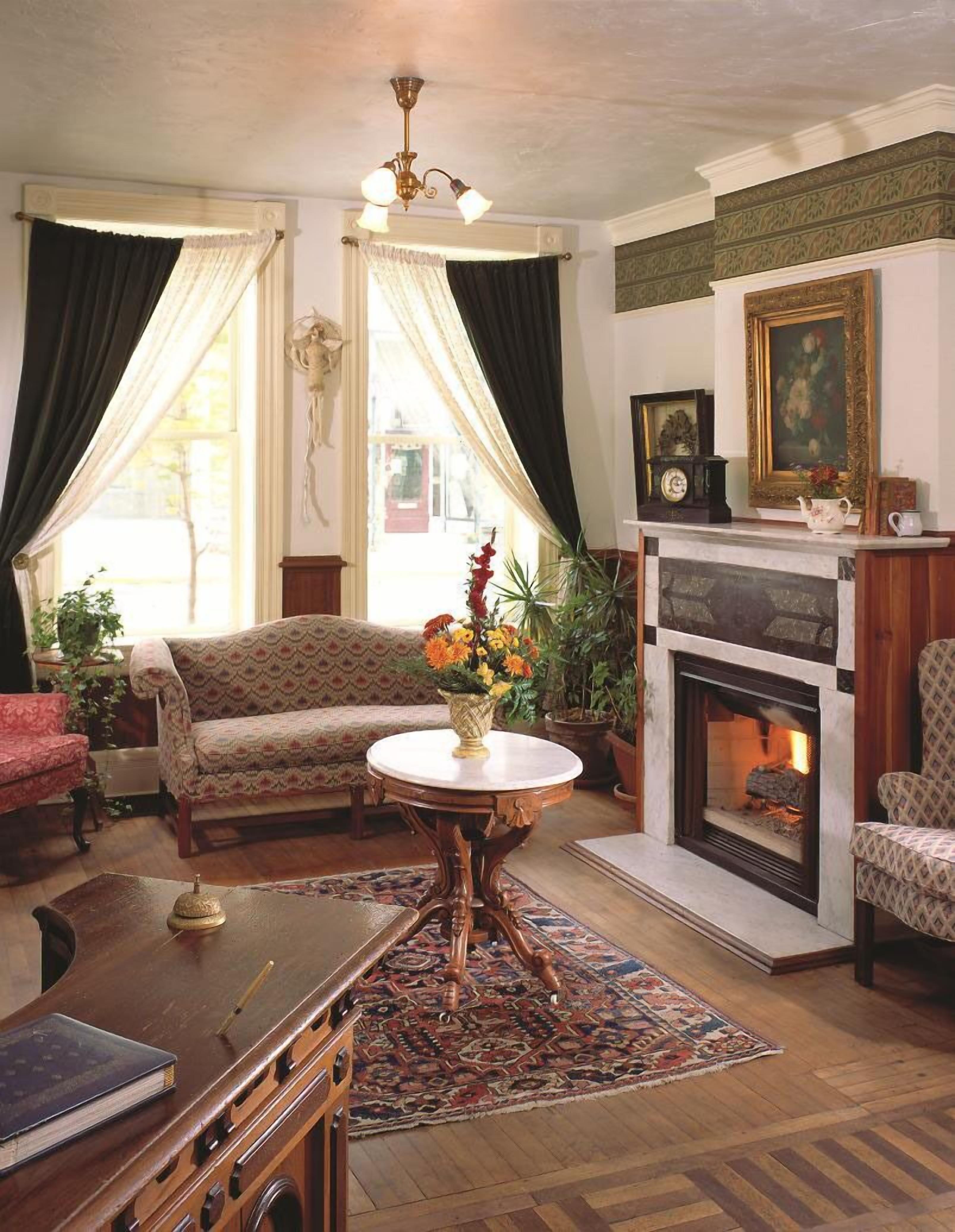 Un salon chaleureux avec une cheminée, un canapé, une table ornée d’un vase de fleurs et un tapis à motifs.