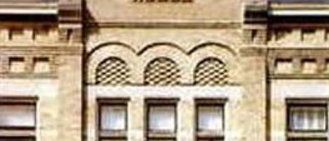 A two-story building with a classic architectural style, featuring a central entrance with a decorative archway and a sign above it.