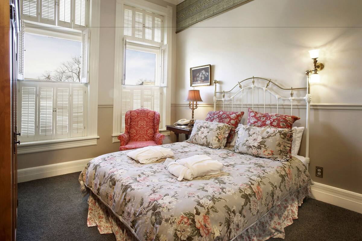 A bedroom with a floral bedspread, a red armchair, and a white metal bed frame.