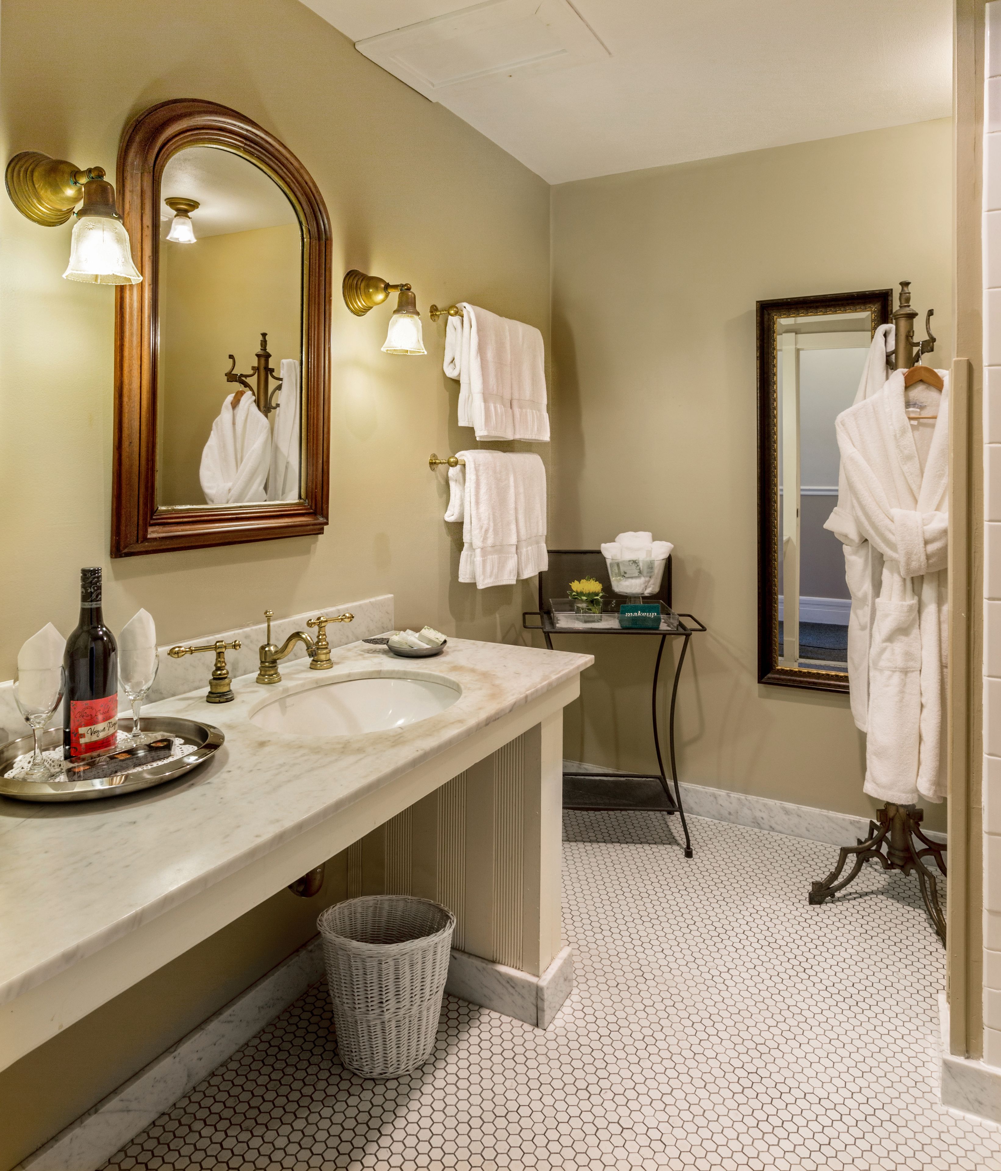 Une salle de bain avec deux lavabos, un grand miroir et une commode sur laquelle se trouvent une bouteille et des verres.