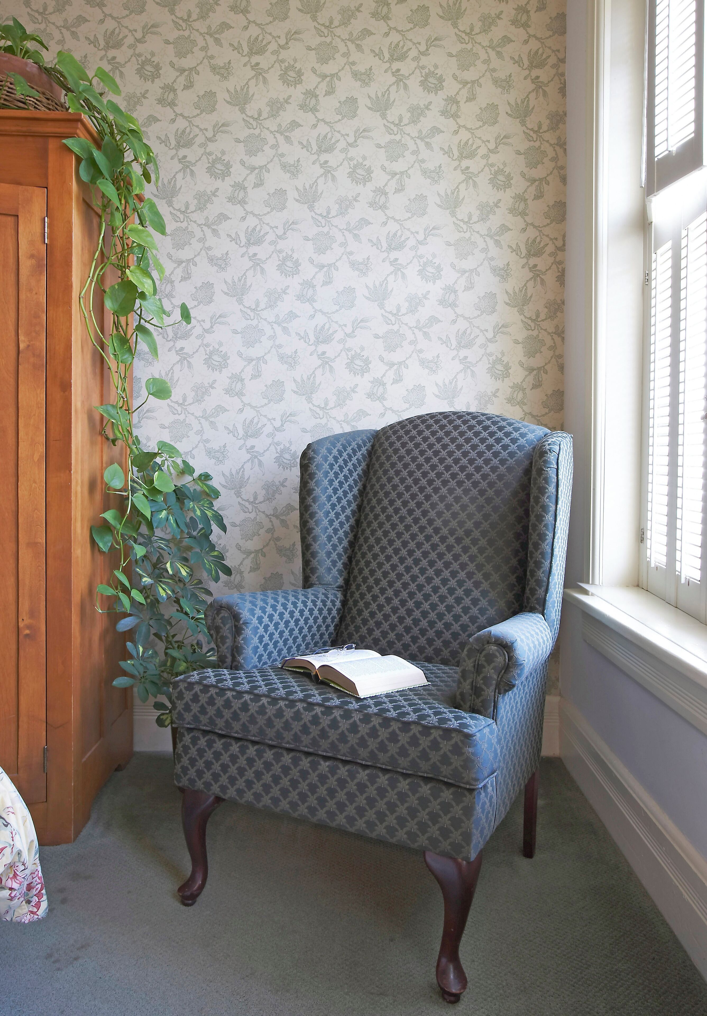 Una silla con tela estampada, un mueble de madera y una pared con papel tapiz floral.