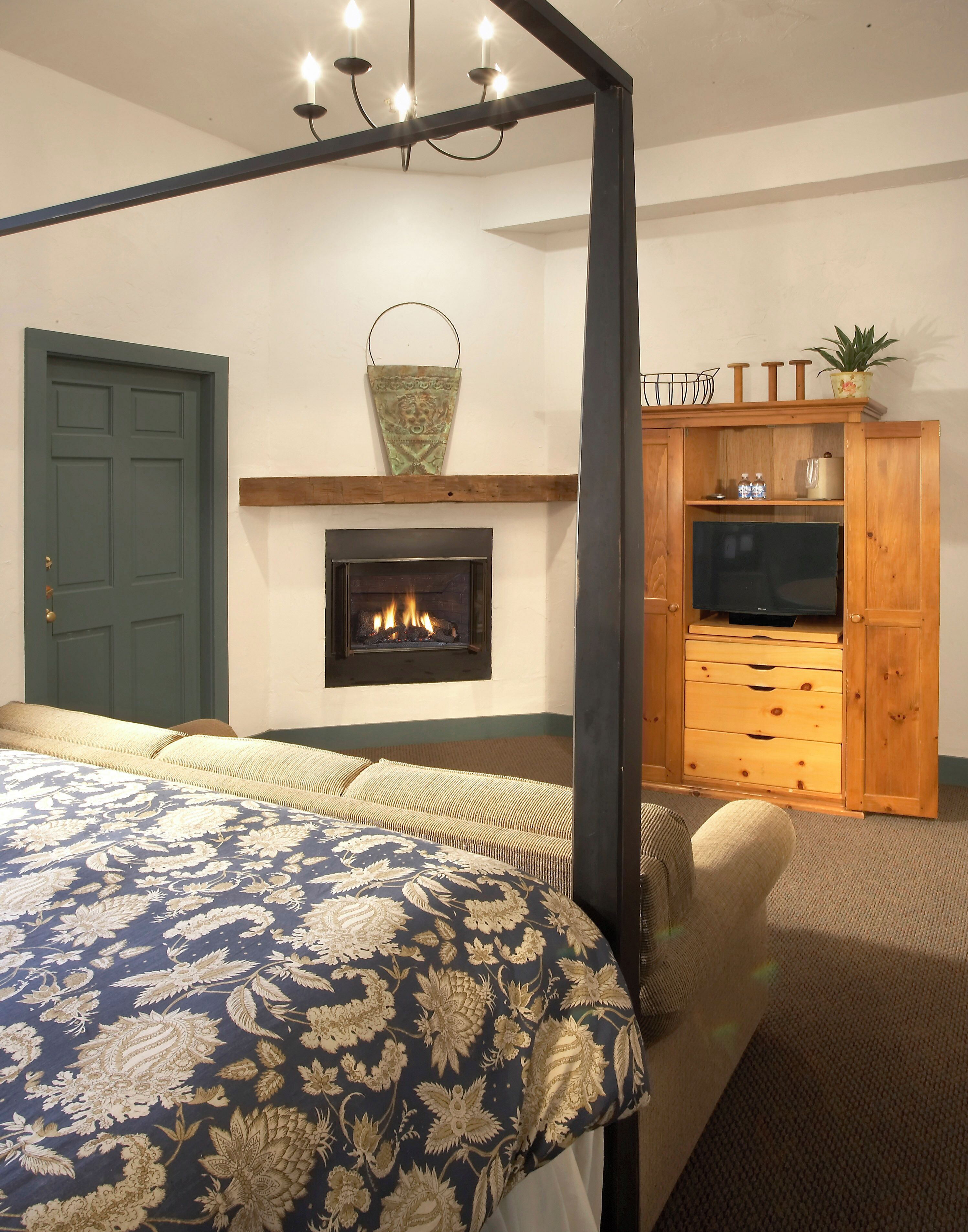 A bedroom with a four-poster bed, a fireplace, a television on a wooden cabinet, and a green door.