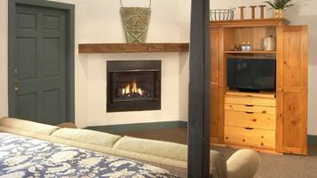 A bedroom with a four-poster bed, a fireplace, a television on a wooden cabinet, and a green door.