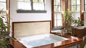 A spacious room with a large bathtub, a wooden headboard, and a brick floor. - Washington House Inn (Cedarburg)