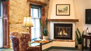 A cozy living room with a stone wall, a fireplace, a comfortable armchair, and a small table with a lamp and a plant. - Washington House Inn (Cedarburg)