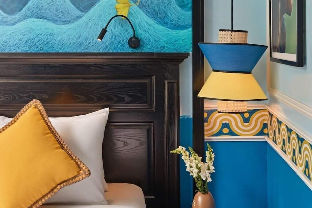 A bedroom with a mural of a bird flying over waves, a bedside lamp, and a vase with flowers.