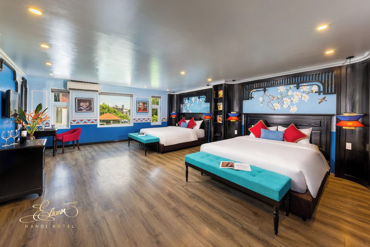 A hotel room with two beds, a desk, and a chair. There are decorative wall art and a large window.