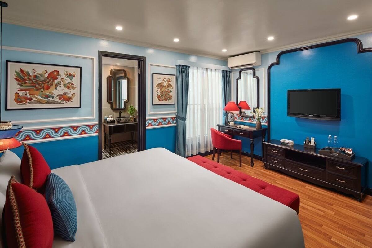 A hotel room with a large bed, a desk with a chair, a TV, and artwork on the walls.
