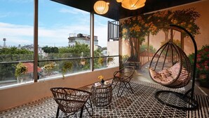 Un balcon avec des fauteuils en osier, un fauteuil suspendu et une vue sur le paysage urbain.