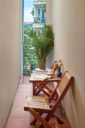 Un balcon étroit avec deux chaises en bois, une petite table, une plante en pot et un vase rempli de fleurs.