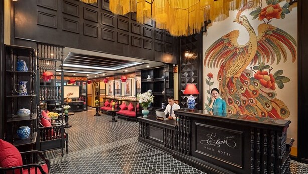 Un hall d’hôtel de style chinois traditionnel, avec un comptoir d’accueil, un espace salon et une grande fresque représentant un paon.