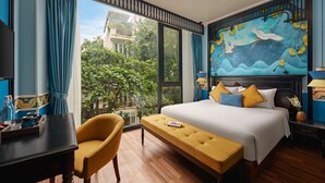 Une chambre d’hôtel avec un grand lit, une banquette, un bureau et une vue sur la verdure.