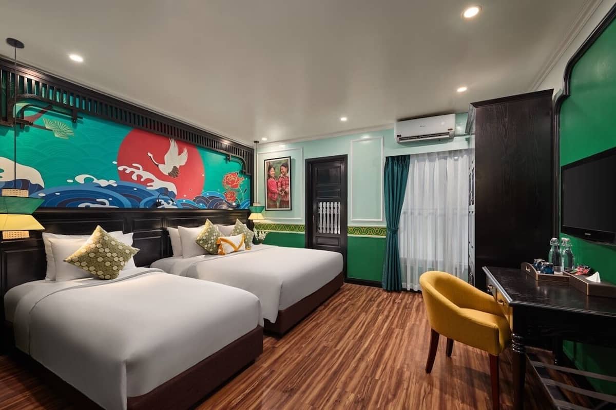 A hotel room with two beds, a desk, a chair, a TV, and a mural on the wall.