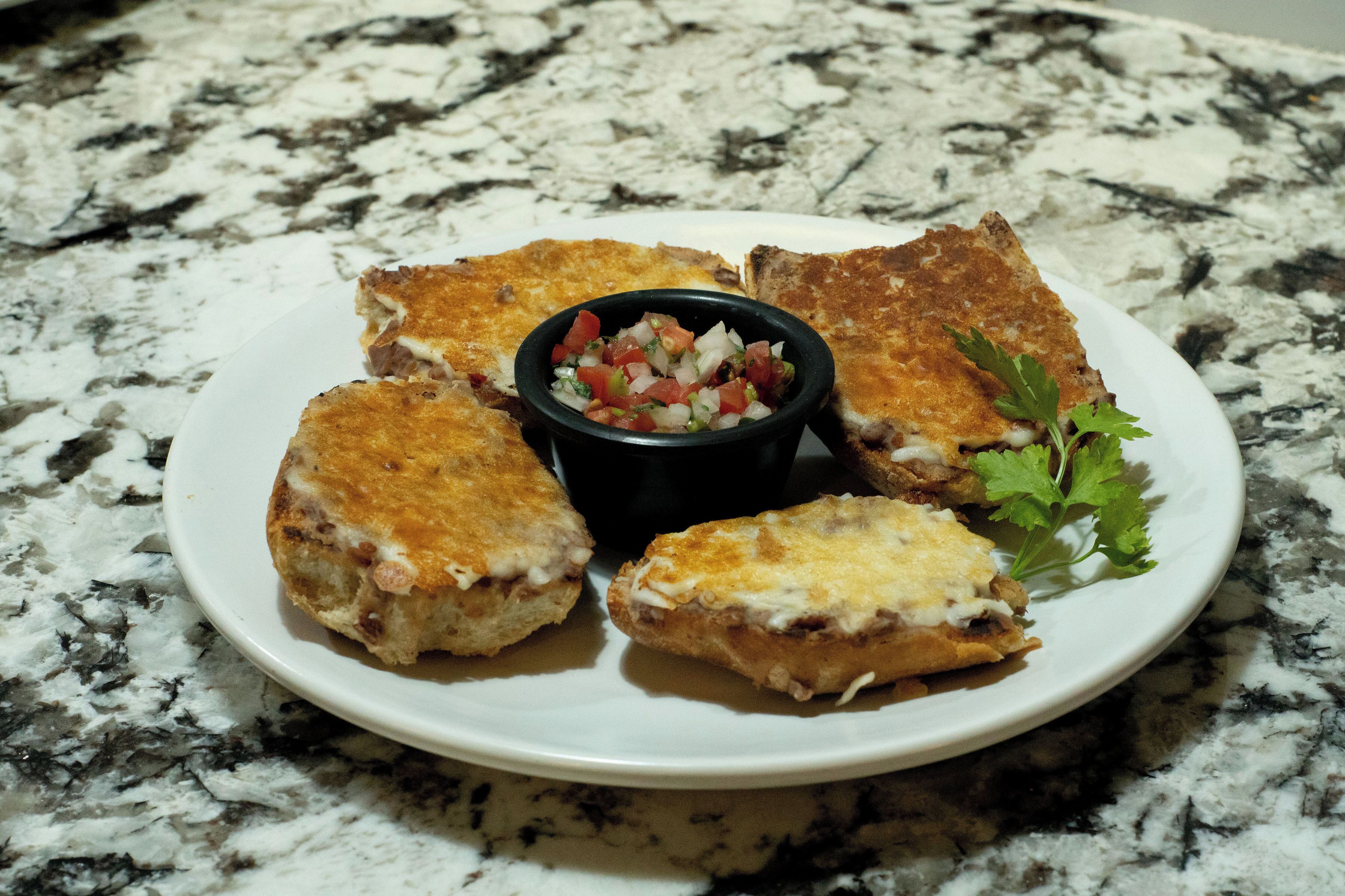 A plate of toasted sandwiches with a side of salsa and a garnish of parsley.