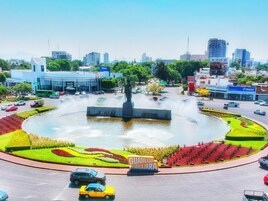Una rotonda con una fuente en el centro, rodeada de jardines ajardinados y una estatua.