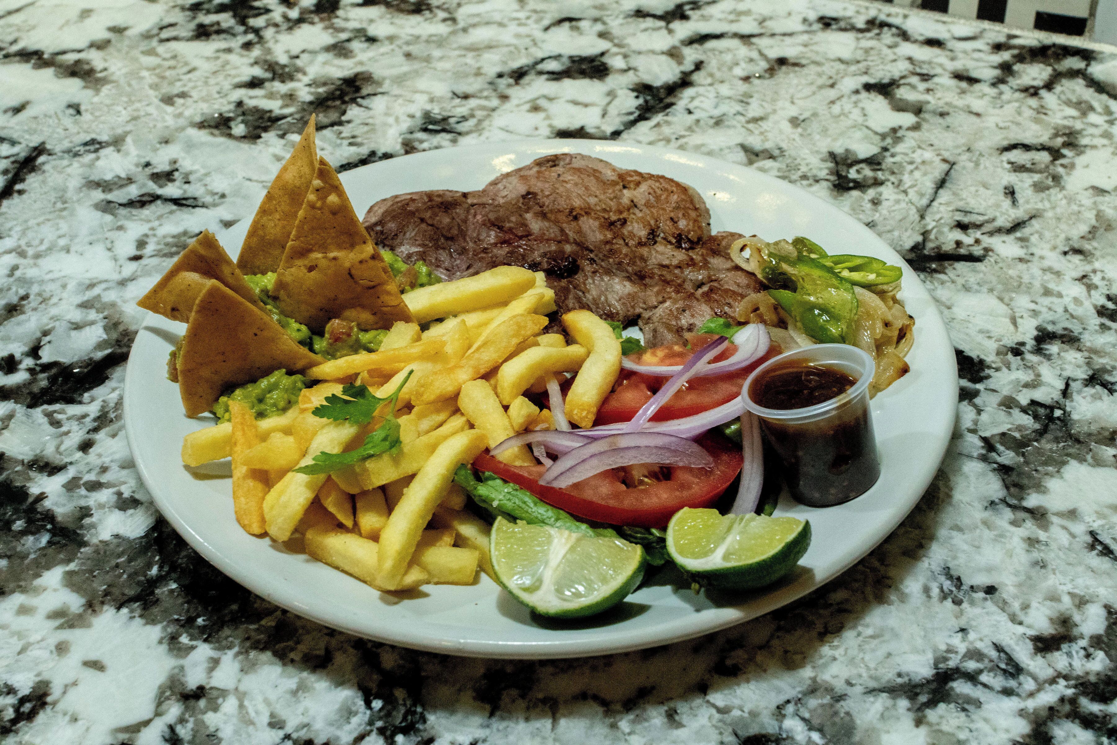 A plate of food including steak, fries, and vegetables on a marble countertop.