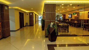 A hotel lobby with a long corridor, wooden walls, and a seating area with tables and chairs.