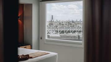 Un dormitorio moderno con cama, mesita de noche y ventana con vistas a la ciudad.