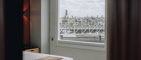Un dormitorio moderno con cama, mesita de noche y ventana con vistas a la ciudad.