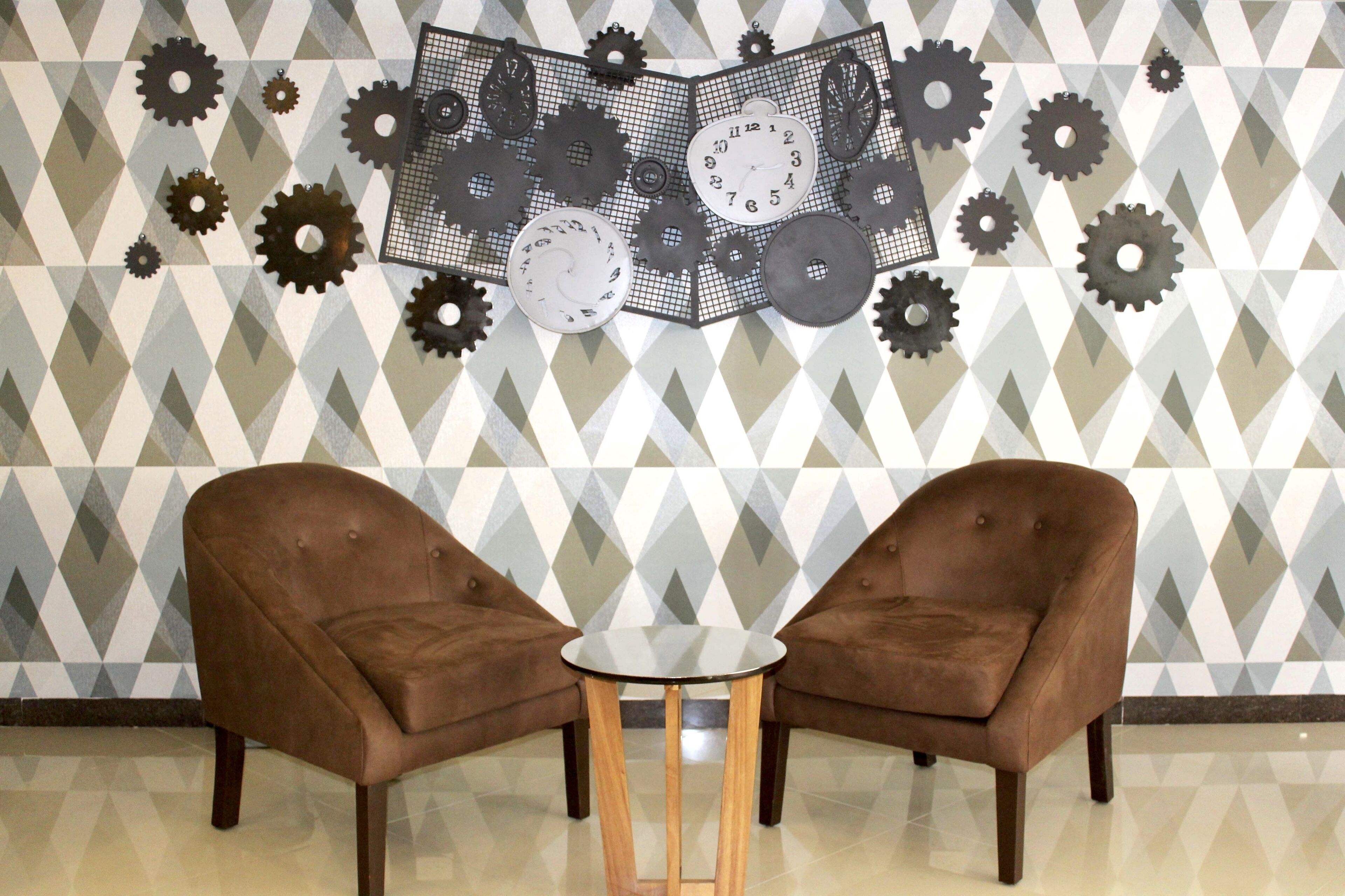 Una habitación con dos sillones marrones enfrentados, una pequeña mesa redonda y una pared decorada con engranajes y relojes.