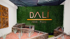 A modern hotel lobby with a green wall and the name 'DALÍ Hotel Plaza' prominently displayed.