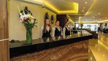 A reception desk with three staff members, a vase of flowers, and a clock on the wall.