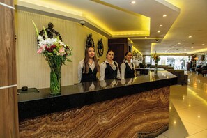 Una recepción con tres empleados, un jarrón de flores y un reloj en la pared.