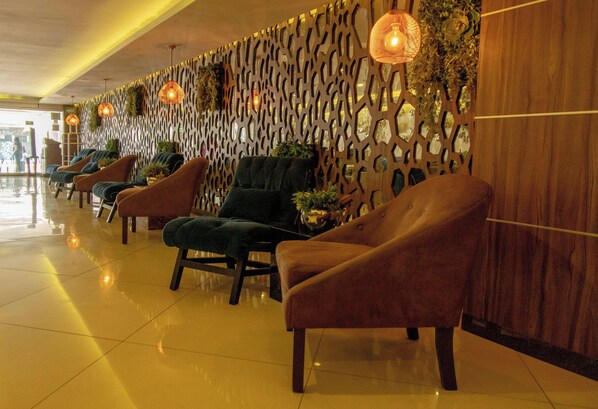 Un vestíbulo de hotel con una fila de sillones cómodos, una pared decorativa con patrones geométricos e iluminación colgante.