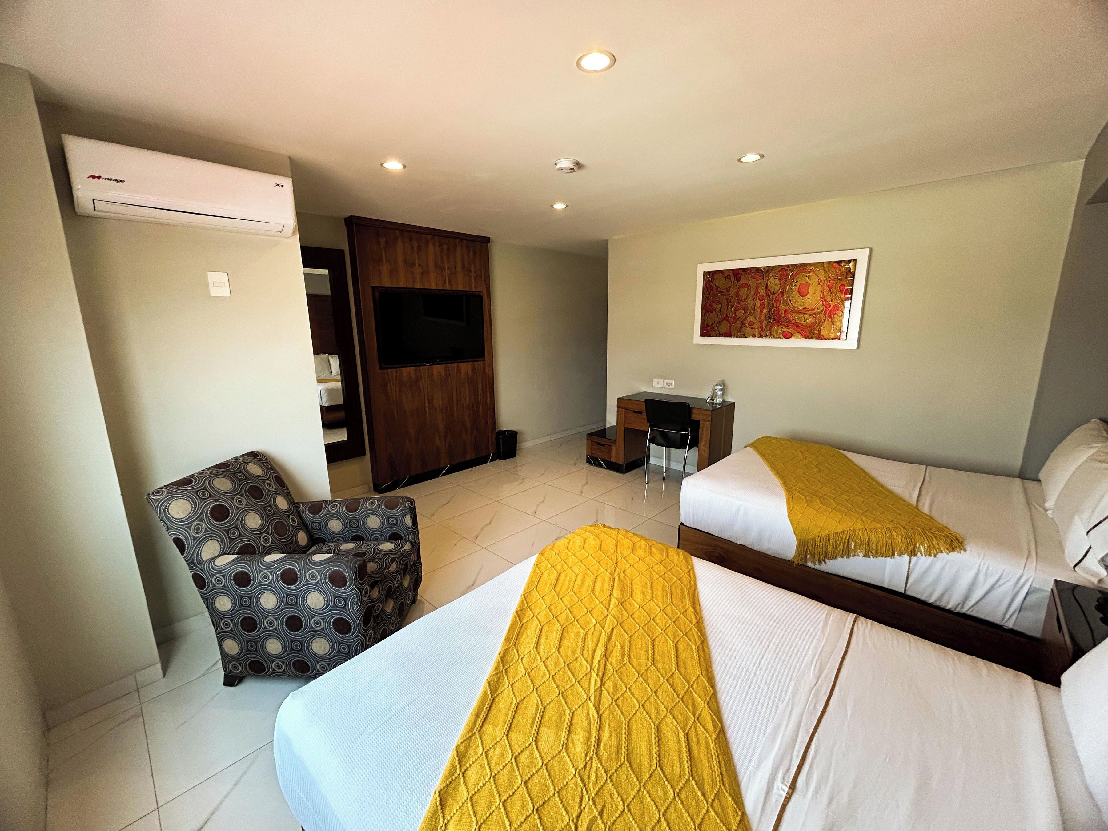 A hotel room with two beds, a desk, a chair, an air conditioning unit, and a television.