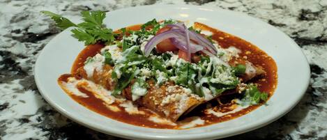 A plate of enchiladas with toppings on a marble countertop.