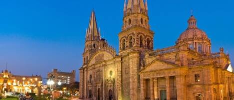 Eine historische Kathedrale mit zwei markanten Türmen und einer großen Kuppel, umgeben von einem Platz mit Bäumen und einer belebten Straße mit Lichtspuren.