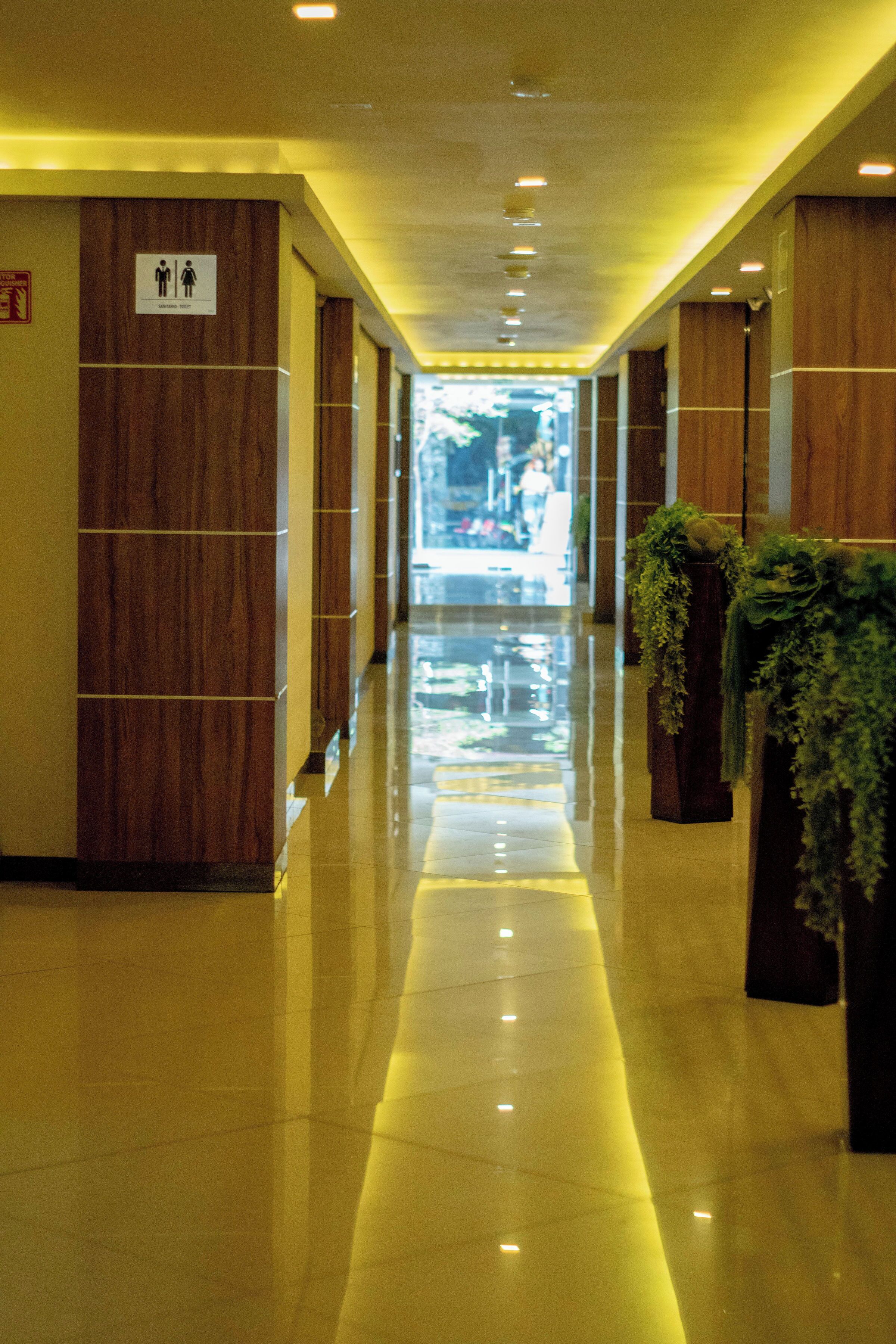 A hotel corridor with wooden paneling, a reflective floor, and potted plants.