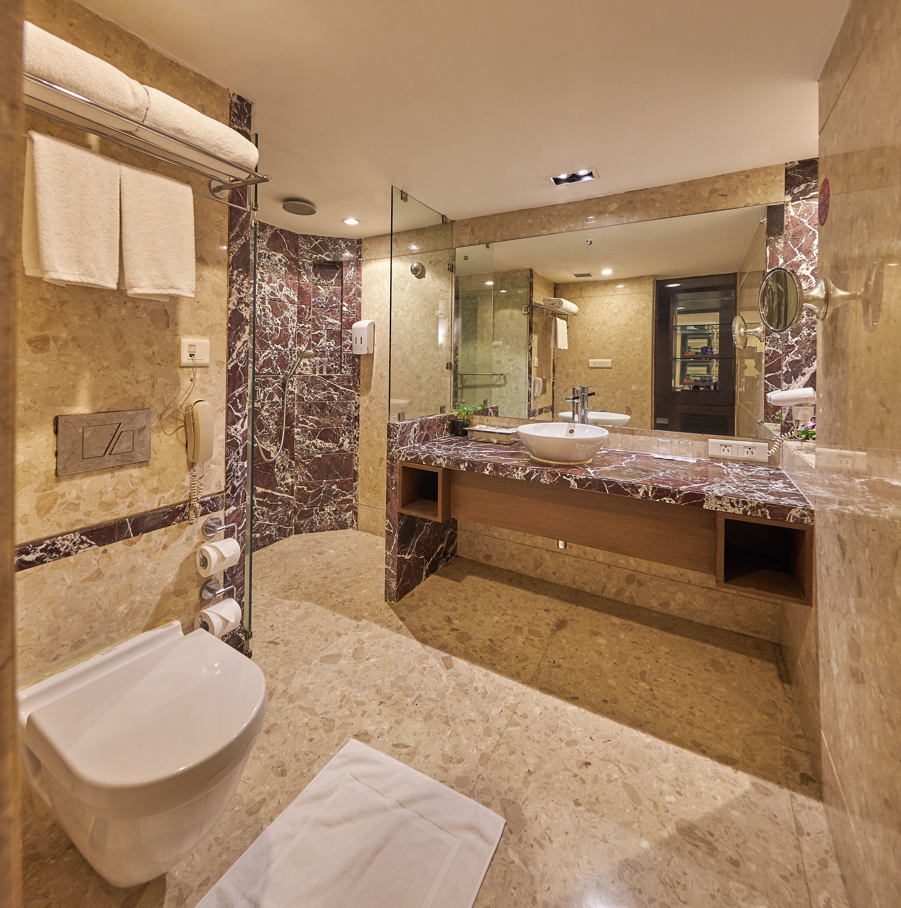 Un baño moderno con tocador de mármol, un espejo grande, una bañera y un inodoro.