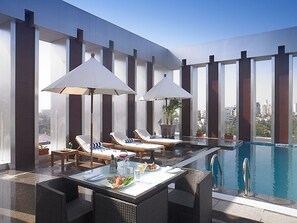 A rooftop pool area with lounge chairs, umbrellas, and a dining table with a meal. - Royal Orchid Central Grazia (Navi Mumbai)
